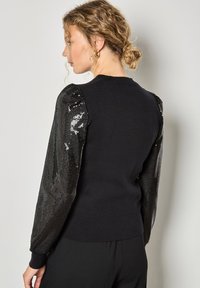 Czarny sweter z cekinowymi bufkami, strukturalnym korpusem, ściągaczami przy mankietach i u dołu. Posiada okrągły dekolt i dopasowany krój.