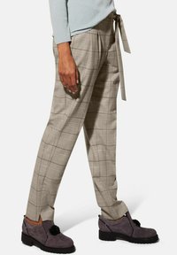 Beige geruite broek met een relaxte pasvorm en een vastgebonden taille-detail. Draag Het met donkergrijze enkellaarsjes met bloemaccenten.