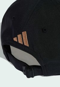 Čierna bejzbalová čiapka s mäkkou textúrou látky. Má tri vyšívané bronzové pruhy na boku. Obsahuje nastaviteľný popruh na zadnej strane.