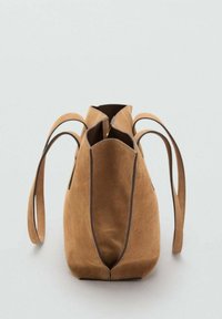 Borsa in suede color marrone chiaro con una consistenza morbida, dotata di manici lunghi e apertura superiore, che mette in evidenza un design minimalista e dettagli marroni.