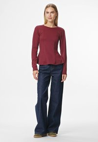 Bordó krāsas garo piedurkņu krekls ar pepluma dizainu, kombinēts ar tumšu, platu džinsu biksēm. Apģērbs ir ar gludu tekstūru un brīvu piegriezumu.