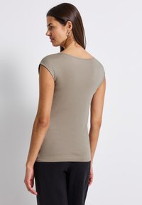 Slim-fit, top s krátkými rukávy v světle taupe tkanině. Hladká textura, kulatý výstřih a jednoduchý design. Nosit s černými kalhotami.