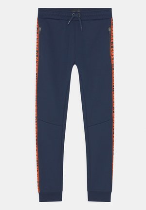 Pantaloni sportivi blu navy con vita con coulisse, strisce laterali arancioni con testo, tasche con zip e polsini a coste. Texture liscia.