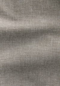 Gros plan d’un tissu beige tissé avec un petit motif carré serré et de subtiles variations de texture.