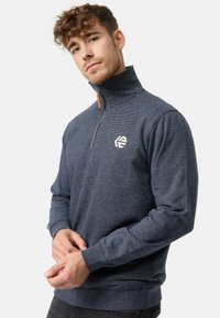 Marineblå, lynlås sweatshirt med høj krave, struktureret stof og kontrasterende logo-detalje på brystet. Ribbet manchetter og kant.