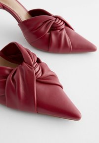 Mules à talons hauts en cuir rouge avec un bout pointu et un design avant noué. Texturé lisse et silhouette épurée.