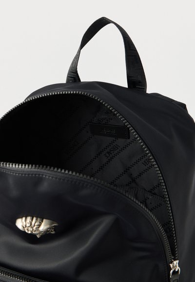 Μαύρο σακίδιο πλάτης με ανοιχτό φερμουάρ που αποκαλύπτει το εσωτερικό ύφασμα τυπωμένο με το μοτίβο "Versace" και ασημένιο έμβλημα με κεφάλι Μέδουσας μπροστά.
