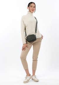 Szara torba na ramię z fakturowanej skóry. Modelka ma na sobie kremowy prążkowany golf, beżowe spodnie o długości przed kostkę oraz białe trampki.