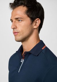 Námořnická polo košile s texturovaným límečkem, tříknoflíkovou légou a kontrastním logem v bílé a oranžové na hrudi. Hladká látka.