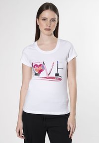 Camiseta blanca de manga corta con un estampado gráfico colorido que presenta la palabra "AMOR" y herramientas de maquillaje en varios colores y texturas.