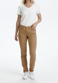 Beiga skinny jeans med midjehöjd och tre framfickor, kombinerade med en figurnära vit V-ringad t-shirt och vita sneakers.