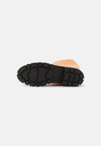 Bota de couro castanho com uma sola de borracha preta texturizada, apresentando sulcos profundos para tração e um cabedal liso.