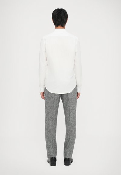 Camicia bianca a maniche lunghe con orlo curvo, abbinata a pantaloni grigi testurizzati. Scarpe nere completano l'outfit. Nessun motivo o accentuazione visibile.