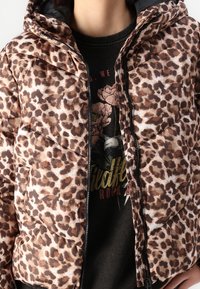 Kurtka puchowa z motywem lamparcim w odcieniach brązu, wyposażona w kaptur, zamek błyskawiczny i boczne kieszenie. Gruba tekstura z pikowanym wzorem.