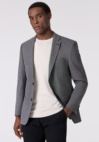 Grau gewobener Blazer mit Reverskragen und zwei Knöpfen, getragen über einem cremefarbenen Rundhalspullover und schwarzen Hosen, mit einer Brusttasche.