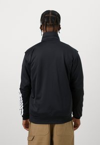 Μαύρο, ελαφρύ μπουφάν με ψηλό γιακά και μακριά μανίκια. Διαθέτει λευκές ρίγες κατά μήκος των μανικιών και υφή λείας ματ.