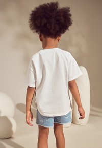 Fehér pamut rövid ujjú póló, világoskék farmer sorttal viselve, amely szív mintás. Puha tapintású, laza szabású. Hátulnézet.