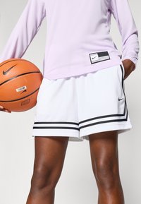 Λευκά μπάσκετ σορτς με μαύρες ρίγες, συνδυασμένα με ένα μωβ πουκάμισο μακρυμάνικο. Ένα μπάλα μπάσκετ κρατιέται στο ένα χέρι.