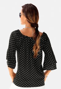 Zwarte blouse met polka dots, off-shoulder decolleté en gerafelde klokmouwen, met een losse fit en een lichtgewicht stof.