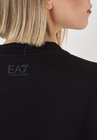 T-shirt nera con scollatura rotonda e una texture liscia. Logo "EA7 Emporio Armani" stampato in contrasto scuro sulla schiena.