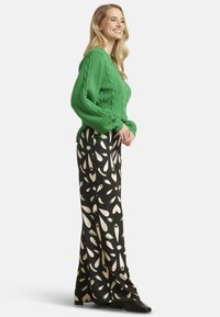 Green knitted sweater with cable pattern, paired with black wide-leg trousers featuring a white and green abstract leaf print. Black heeled boots.