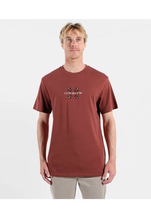 T-shirt en coton bordeaux à manches courtes, col rond, avec un logo brodé central représentant une étoile. Texture lisse, coupe décontractée.