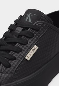 Baskets noires texturées Calvin Klein avec lacets noirs, logo CK visible sur la languette et étiquette Calvin Klein sur le côté.