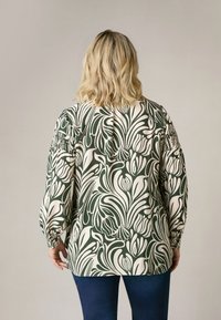 Blusa verde e crema con motivo floreale, maniche a sbuffo e vestibilità rilassata. Presenta dettagli arricciati vicino ai polsini.