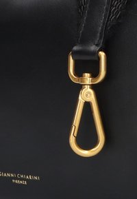 Schwarze Lederhandtasche mit einem goldenen Metallschloss und einem geformten, strukturierten Tragegurt. Das Schloss verfügt über einen federbelasteten Schnappmechanismus.