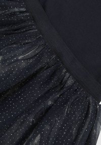 Fekete szoknya textúrált derékrésszel és ezüst pöttyökkel díszített, rétegezett tüllből, ami lágy, áramló sziluettet teremt.