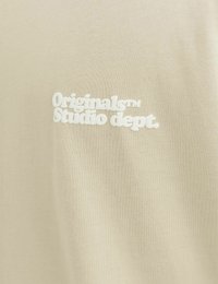 Beige short-sleeve shirt featuring a textured cotton fabric and a white embroidered logo reading "Originals™ Studio dept."
