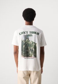 White cotton t-shirt featuring a cactus graphic and text on the back. Short sleeves, relaxed fit, and simple design.