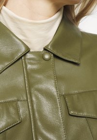 Veste en cuir vert olive avec un col, dotée d'une fermeture à bouton et de deux poches poitrine, texture lisse et lignes épurées.