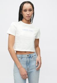 Fehér pamut, rövid ujjú, rövidített póló, amelyen világosszürke "Calvin Klein New York City" felirat található a mellkason.