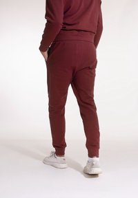 Burgundy sweatpants med en avsmalnande design, elastisk midja och sidfickor. Bärs med vita sneakers. Slät tygstruktur.