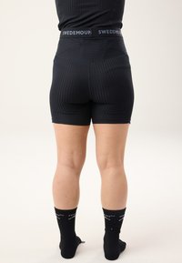 Black fitted shorts with ribbed texture and a high waistband featuring the brand name "SWEDEMOUN" in white. Black ankle socks with logo.