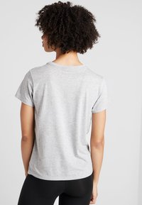 Šedé tričko s krátkým rukávem a kulatým výstřihem. Hladká látka, volný střih a bez viditelných vzorů či grafik. Nošeno s černými legínami.