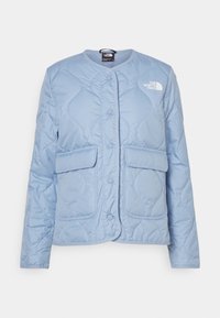 Jasnoniebieska pikowana kurtka z okrągłym dekoltem, zatrzaskami i dwoma naszywanymi kieszeniami z przodu. Z lewej górnej strony małe logo.