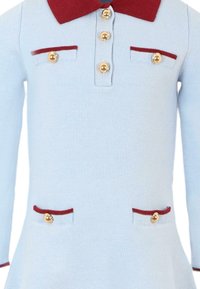 Abito lavorato a maglia blu chiaro con colletto rosso, bottoni dorati e due tasche frontali rifinite con bordi rossi. Corpino aderente che si allarga in vita.