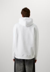 Witte hoodie met een zachte textuur en geribbelde manchetten. Eenvoudig ontwerp, zonder opvallende patronen of accenten, gezien vanaf de achterkant.