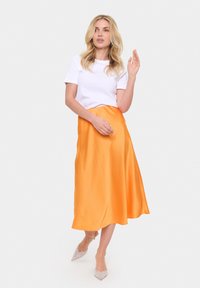 Witte blouse met korte mouwen gecombineerd met een vloeiende oranje satijnen midi rok en beige glinsterende puntige hakken, met een gladde textuur en een lichte val.