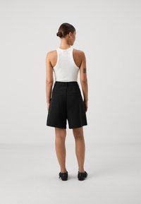 Svarta höga shorts med breda ben och bältesöglor, matchade med en vit figurnära linne. Slät tyg, minimalistisk design, inga synliga mönster.
