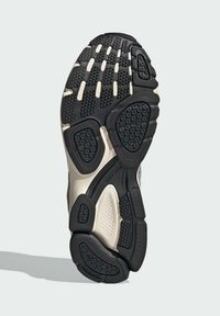 Black rubber sole with textured grip pattern, featuring cream-colored accents and a torsion system detail. Curved shape for support.