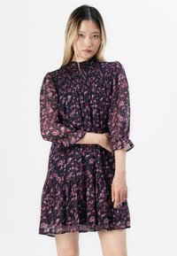 Blomstertrykt kjole i marineblå og rosa. Har en smocket bodice, lange gjennomsiktige ermer og en lagdelt, volangkant. Lett materiale.