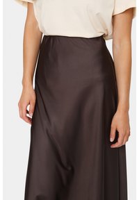 Brun satin kjol med en mjuk textur, hög midja och flödande design, parat med en ljusfärgad topp. Fokusera på tyg och silhuett.