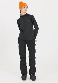 Svart zip-up jacka med hög krage, ihopparad med svarta utomhusbyxor; orange mössa; elegant, funktionell design, lämplig för aktiv användning.