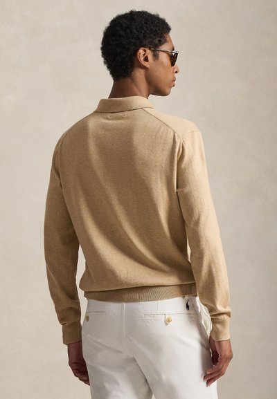 Maglione beige a maglia con collo polo, caratterizzato da una vita aderente e polsini a costine. Abbinato a pantaloni bianchi con dettagli a bottoni.