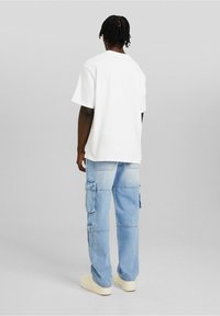 Vitt t-shirt med korta ärmar kombinerad med ljusblå cargobyxor med flera fickor och en ledig passform. Creamfärgade sneakers kompletterar looken.