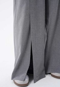 Grijze broek met wijde pijpen, gemaakt van een textuurstof, met een zijscheur en een licht uitlopende vorm, gecombineerd met lichtgekleurde sneakers.