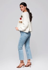 Vit kortärmad tröja med blommiga applikationer, ljusblå högmidjade jeans och bruna remsandaler. Slät textur, avslappnad passform.
